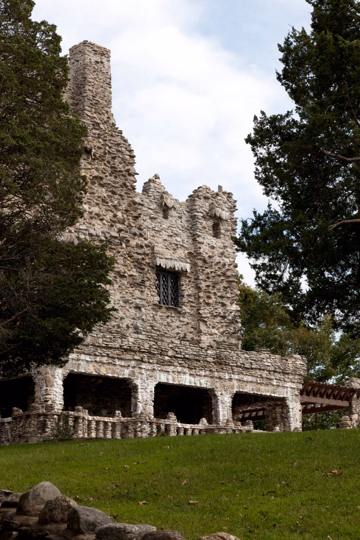 Stone castle tower rising above a lawn and evergreen trees